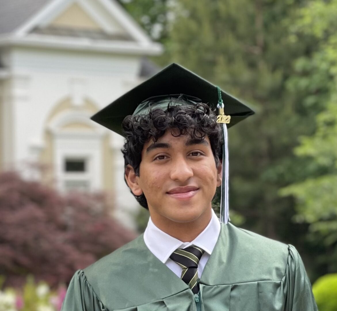 A young man in graduation attire standing outside.