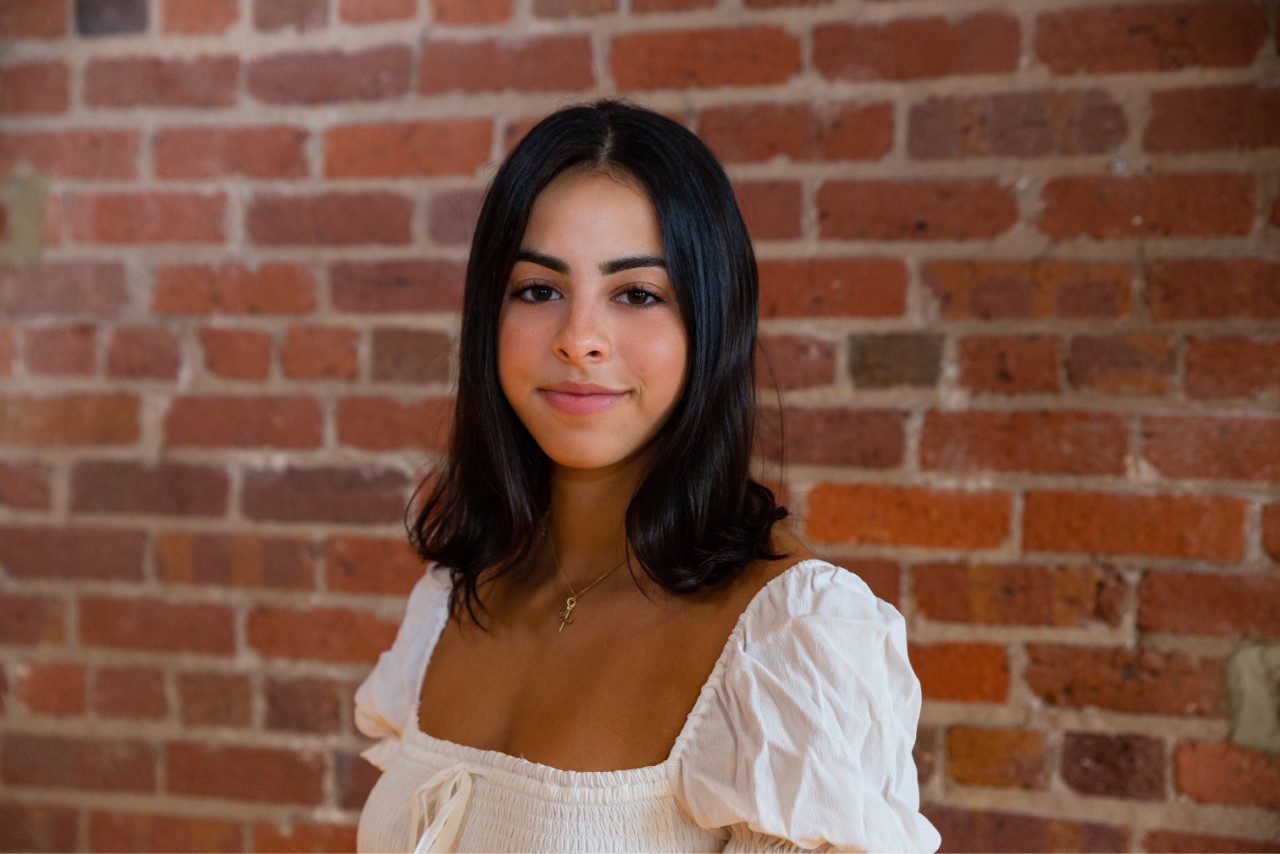 A woman in white shirt standing next to brick wall.