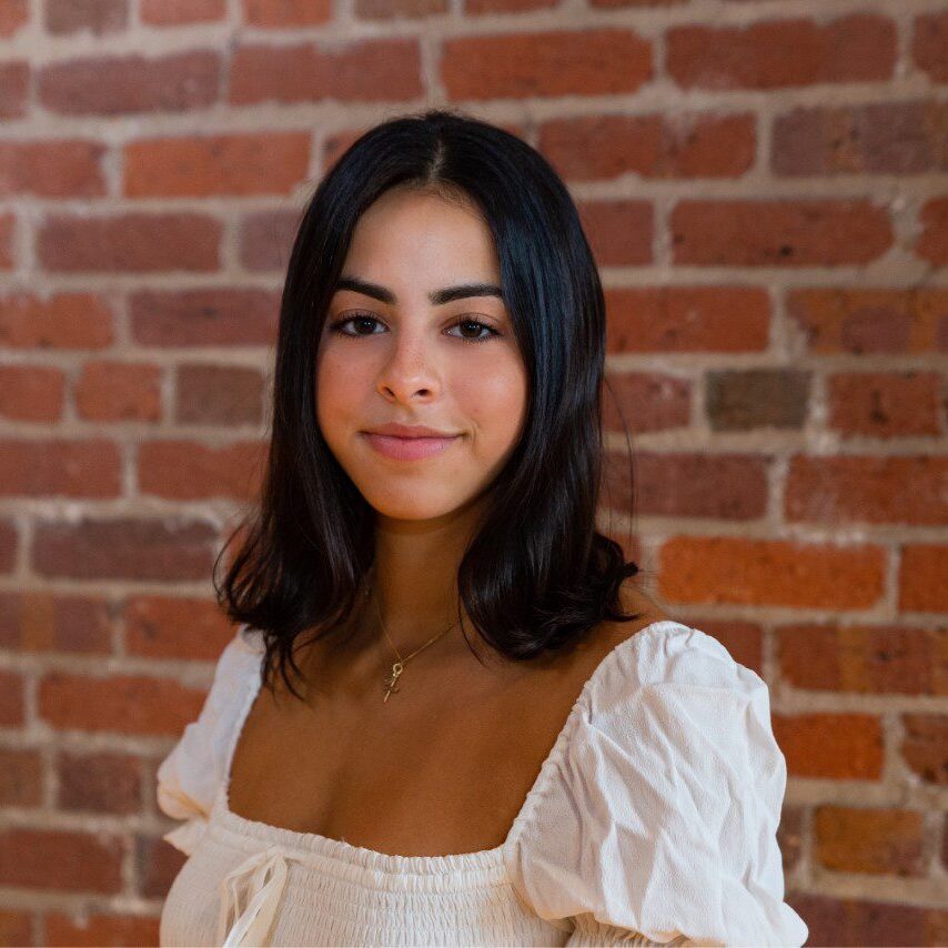 A woman in white shirt standing next to brick wall.