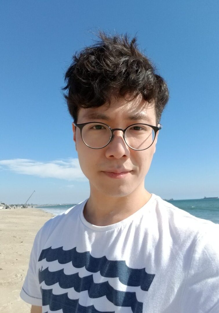 A man with glasses standing on the beach.