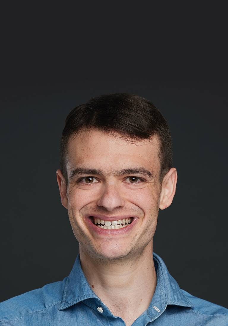 A man with short hair and a blue shirt is smiling.